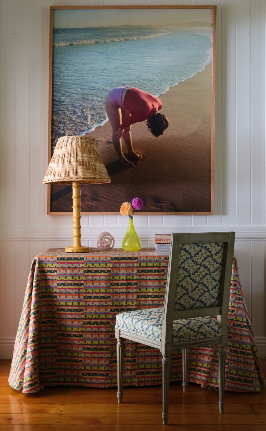 A cluttered desk and chair stand in front of a wall with a large framed print of a woman at the beach.