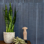 Plants and a statue stand in front of a wall papered in an irregular grid pattern in charcoal on a navy field.