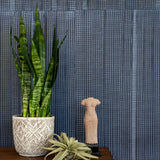 Plants and a statue stand in front of a wall papered in an irregular grid pattern in charcoal on a navy field.