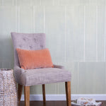 A chair and some books stand in front of a wall papered in an irregular grid pattern in light gray on a cream field.