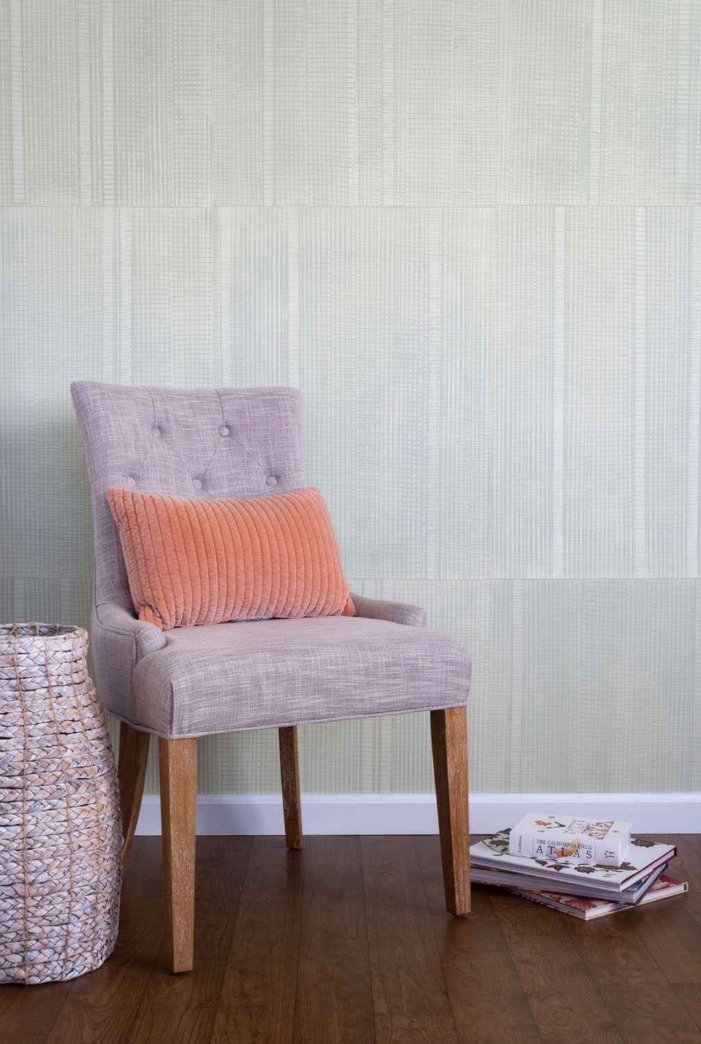 A chair and some books stand in front of a wall papered in an irregular grid pattern in light gray on a cream field.