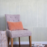 A chair and some books stand in front of a wall papered in an irregular grid pattern in light gray on a cream field.