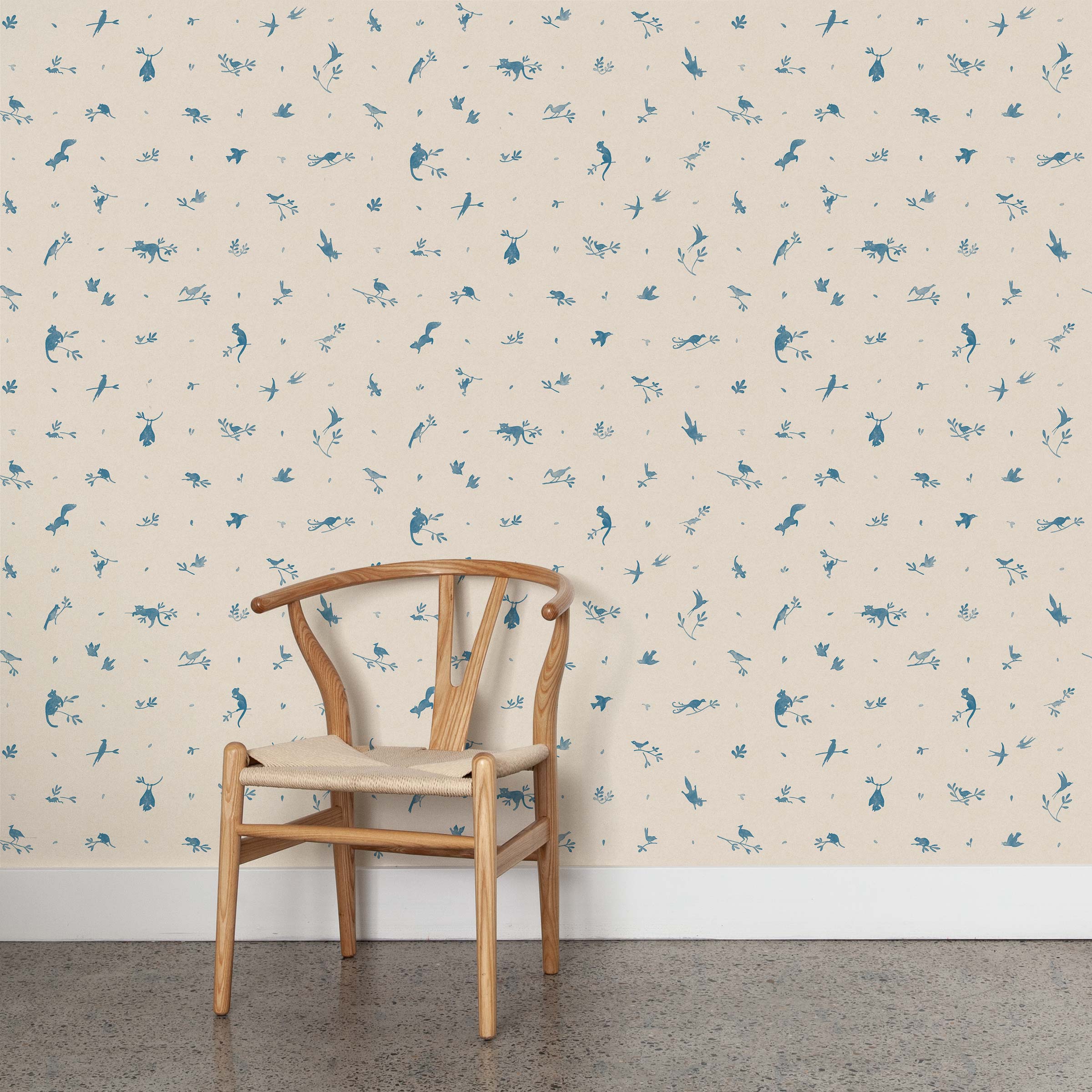 A wooden chair stands in front of a wall papered in a playful animal and branch print in blue on a cream field.