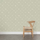 A wooden chair stands in front of a wall papered in a playful animal and branch print in white on a sage field.