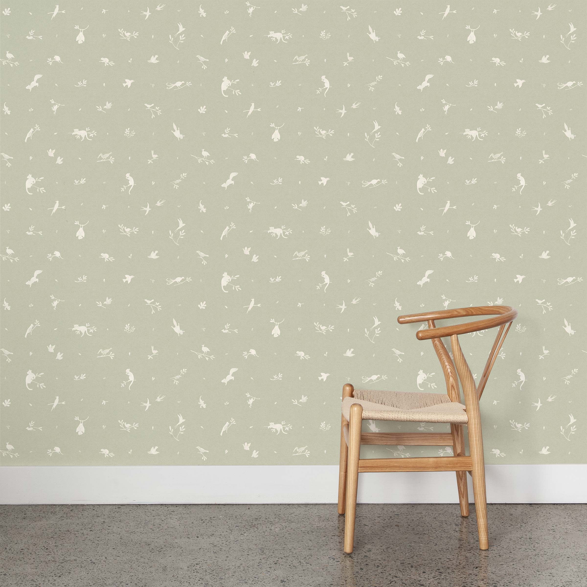 A wooden chair stands in front of a wall papered in a playful animal and branch print in white on a sage field.