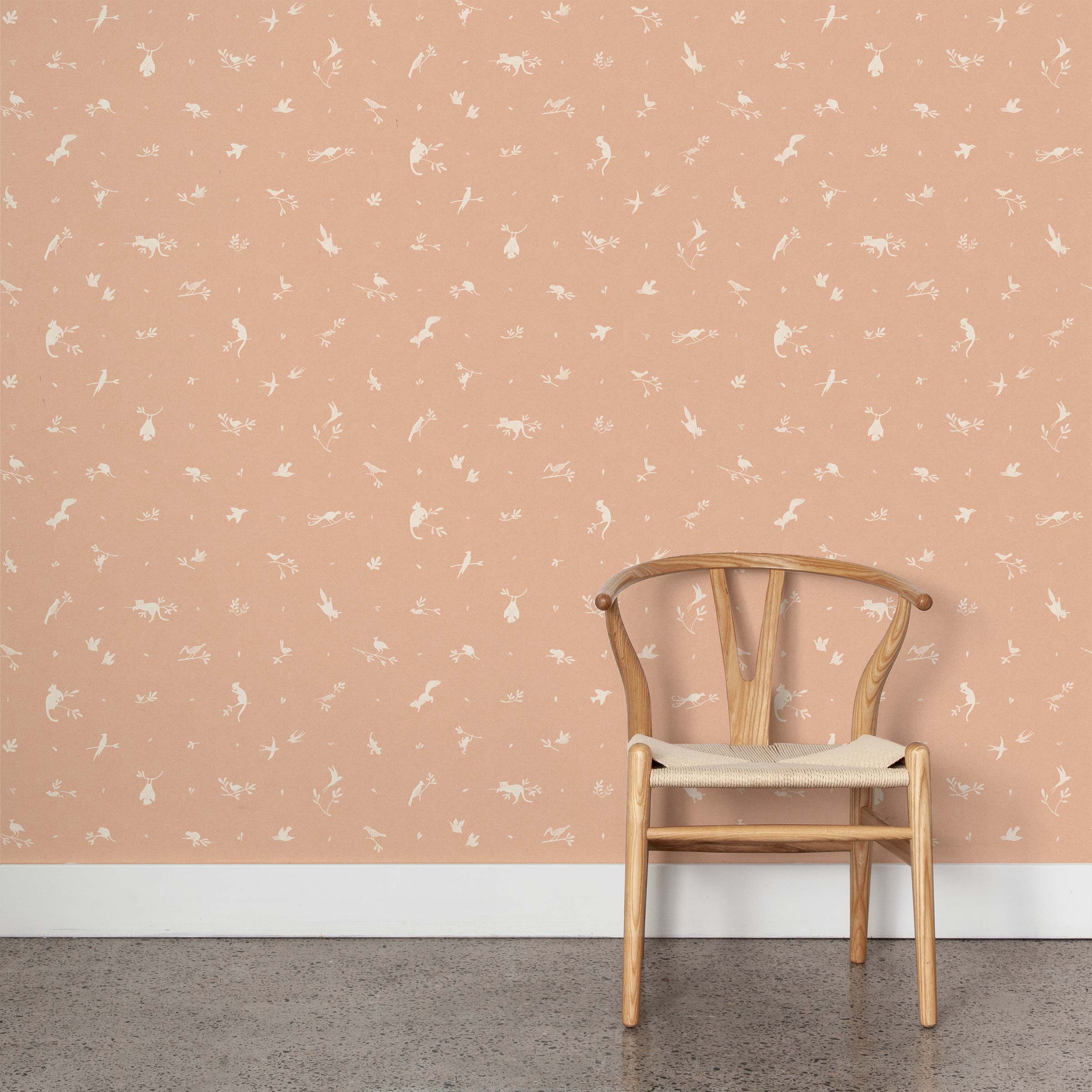 A wooden chair stands in front of a wall papered in a playful animal and branch print in white on a coral field.