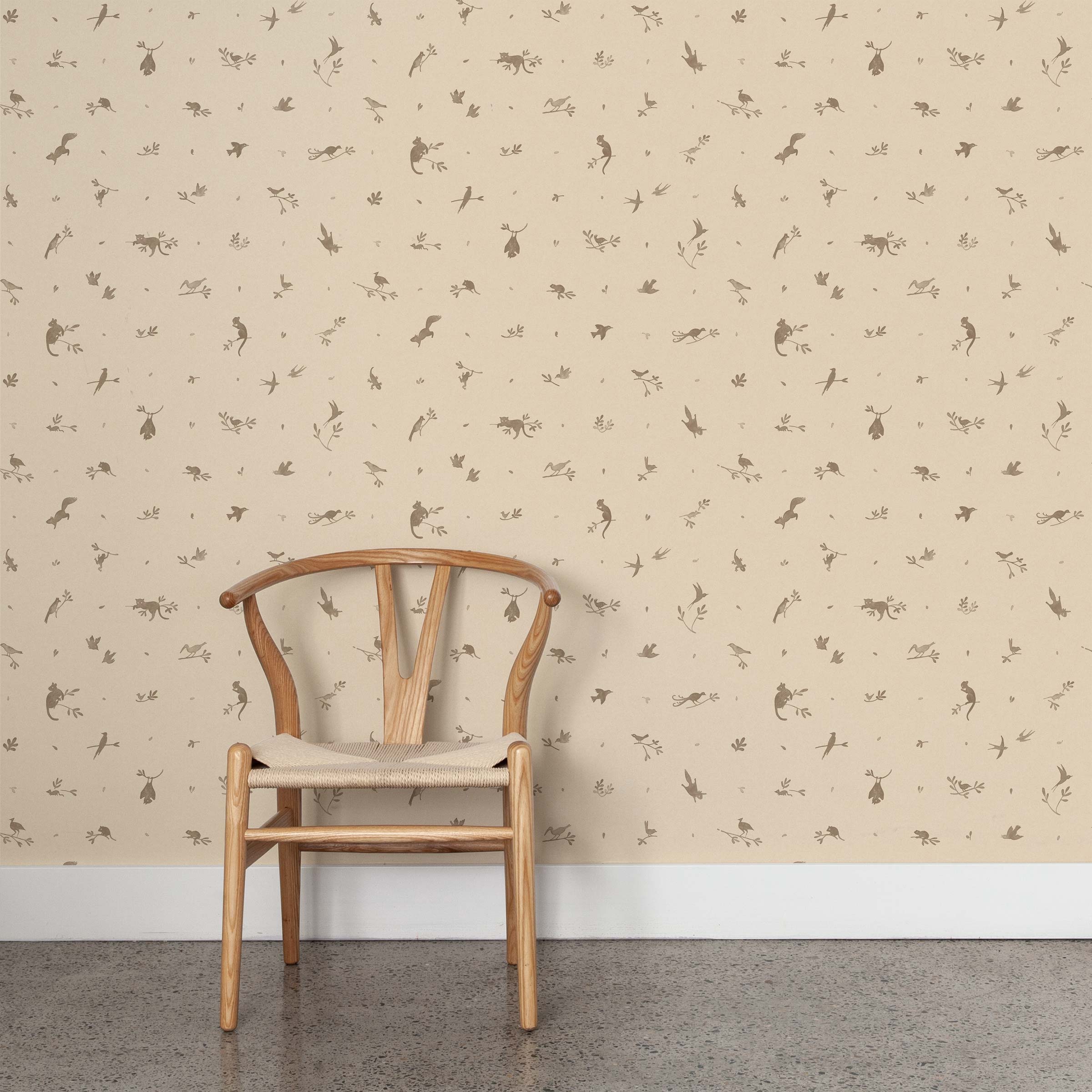 A wooden chair stands in front of a wall papered in a playful animal and branch print in brown on a cream field.