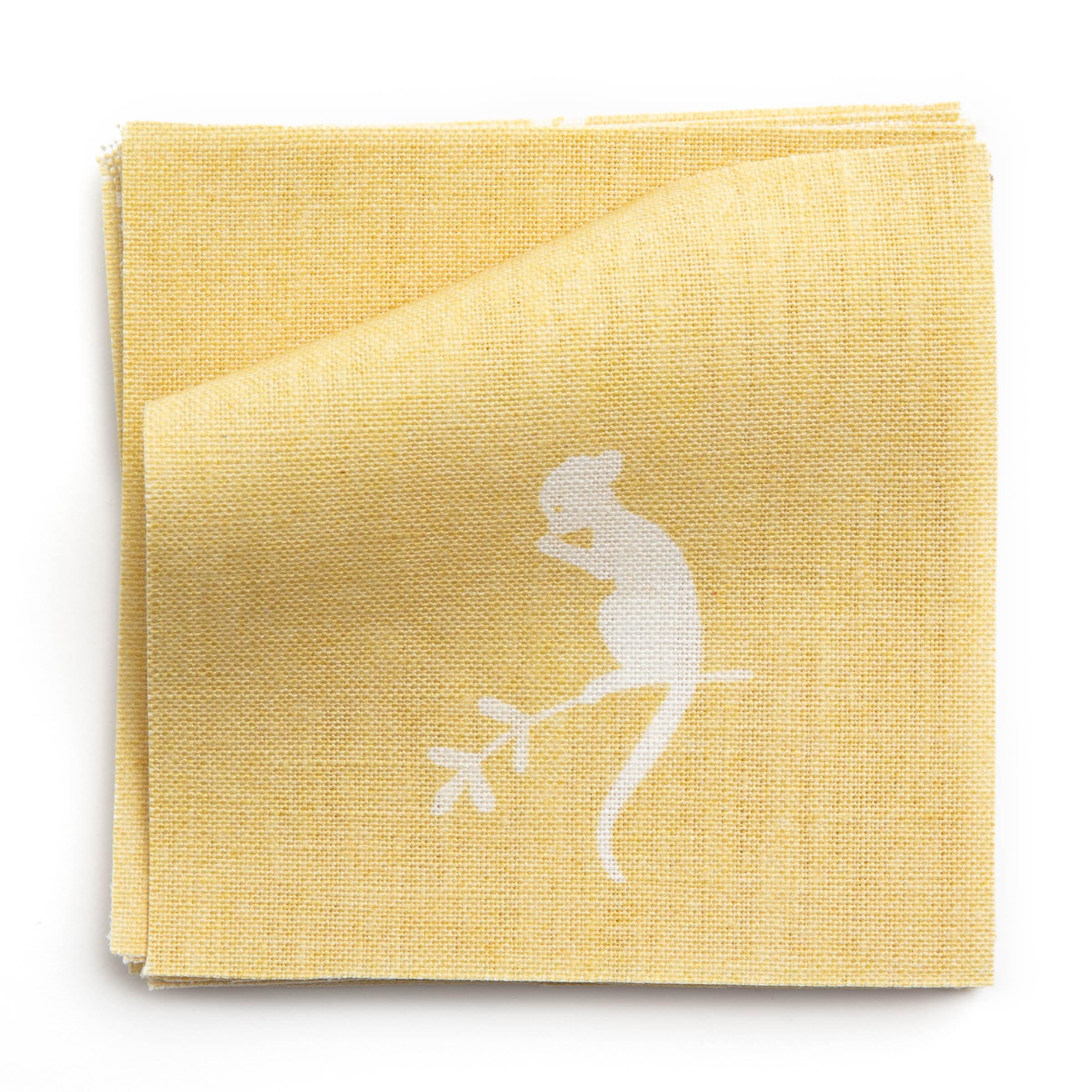 A stack of fabric swatches in a playful animal and branch print in white on a yellow field.