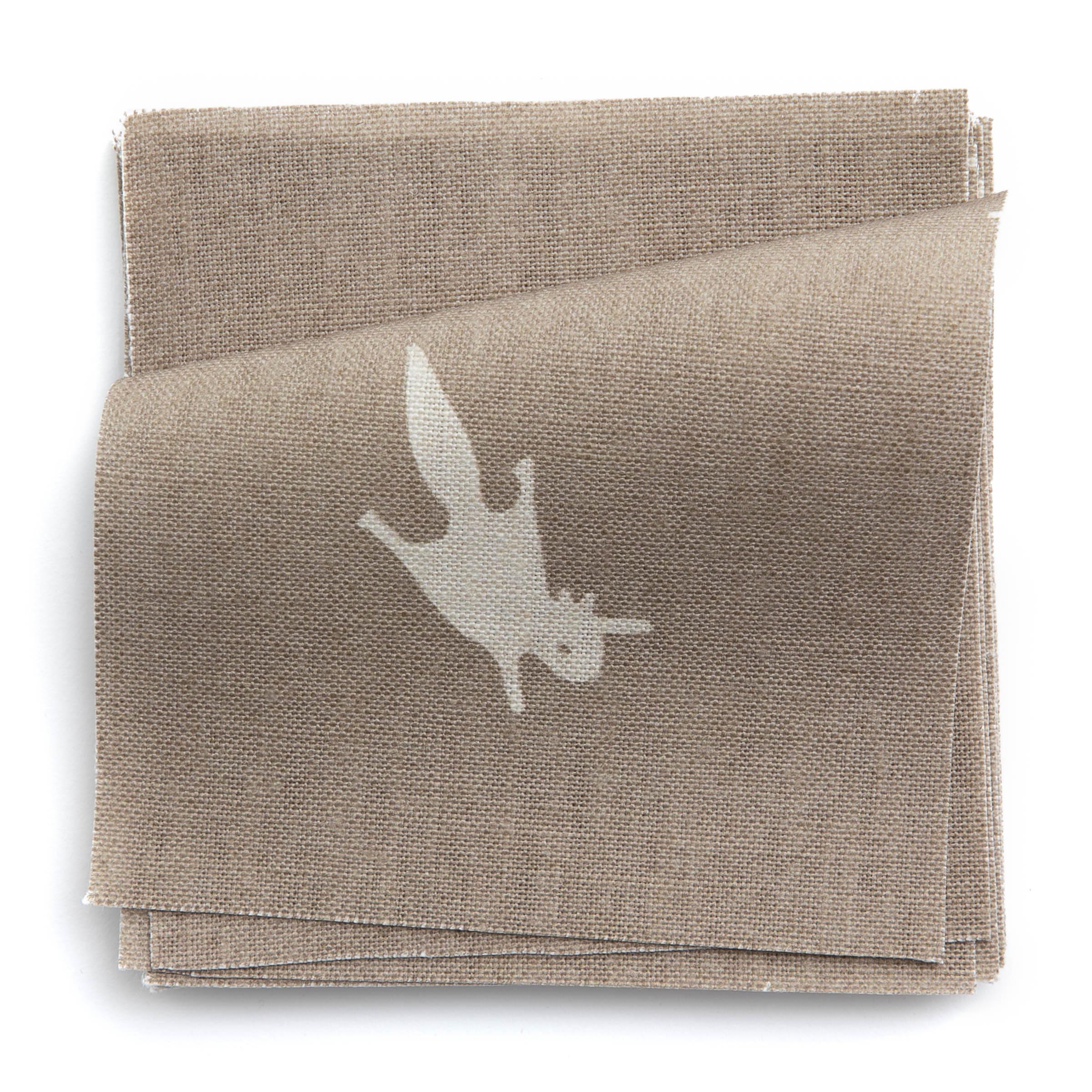 A stack of fabric swatches in a playful animal and branch print in cream on a brown field.