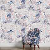 An armchair stands in front of a wall papered in an animal and tree branch print in blue, gray, red and cream.