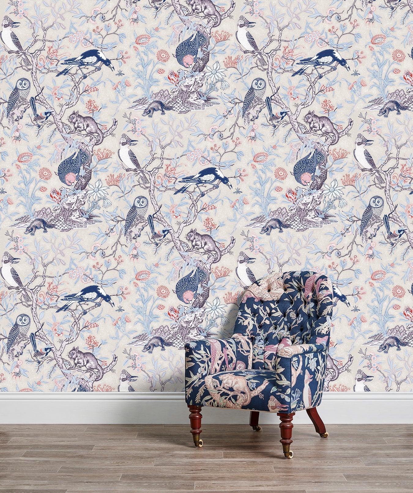 An armchair stands in front of a wall papered in an animal and tree branch print in blue, gray, red and cream.