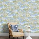 Armchair and end table in front of a wall papered in a painterly tree print in cream, green and light blue.