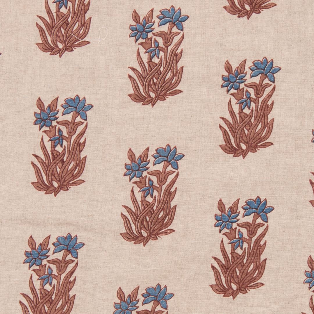 Detail of fabric in a repeating floral grid in blue and rust on a cream field.