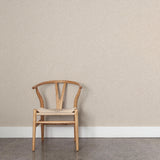 A wooden chair stands in front of a wall papered in a small-scale dot and dash pattern in tan and white on a cream field.