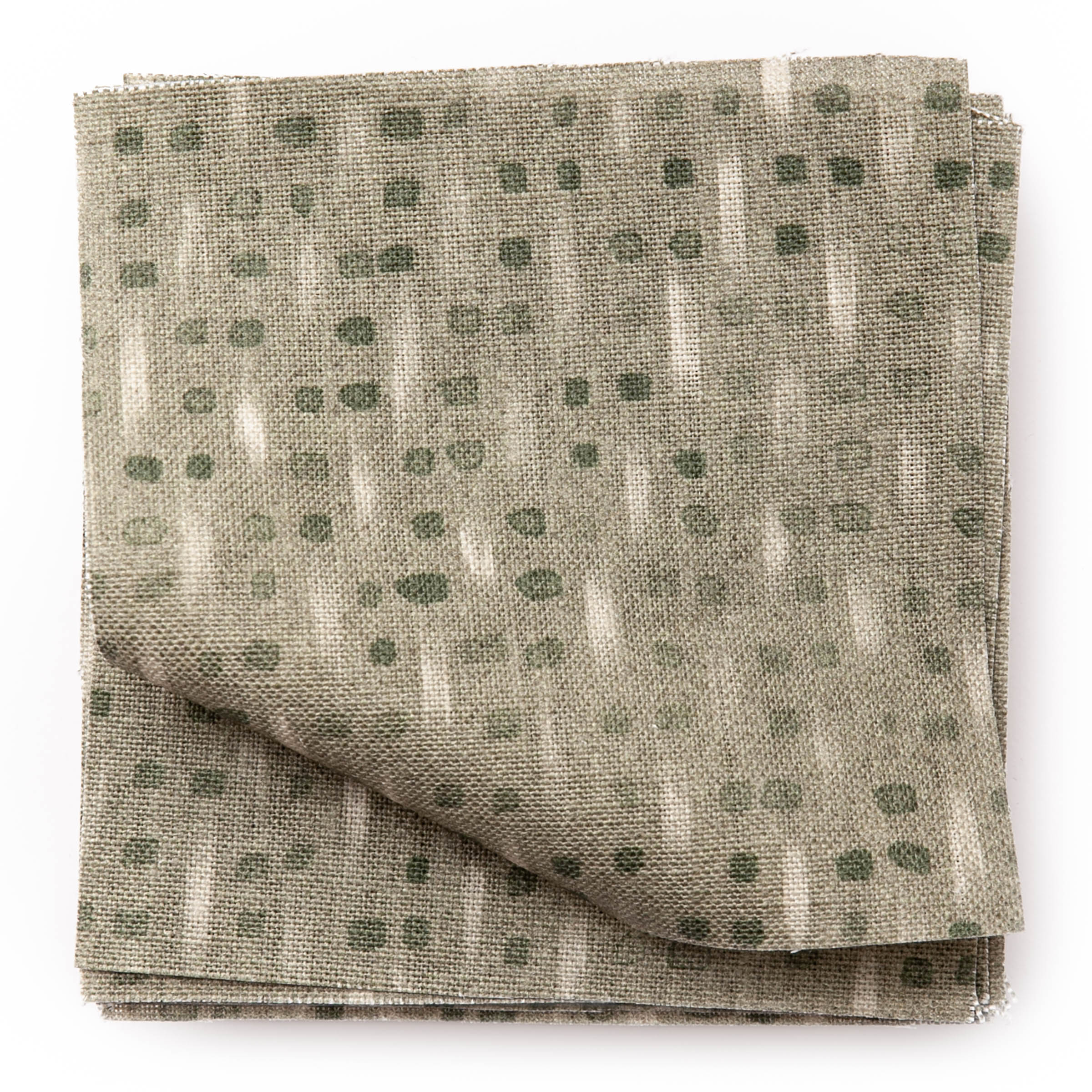 A stack of fabric swatches in a small-scale dot and dash pattern in shades of cream and green on a sage field.