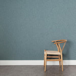 A wooden chair stands in front of a wall papered in a small-scale dot and dash pattern in shades of blue on a blue-gray field.