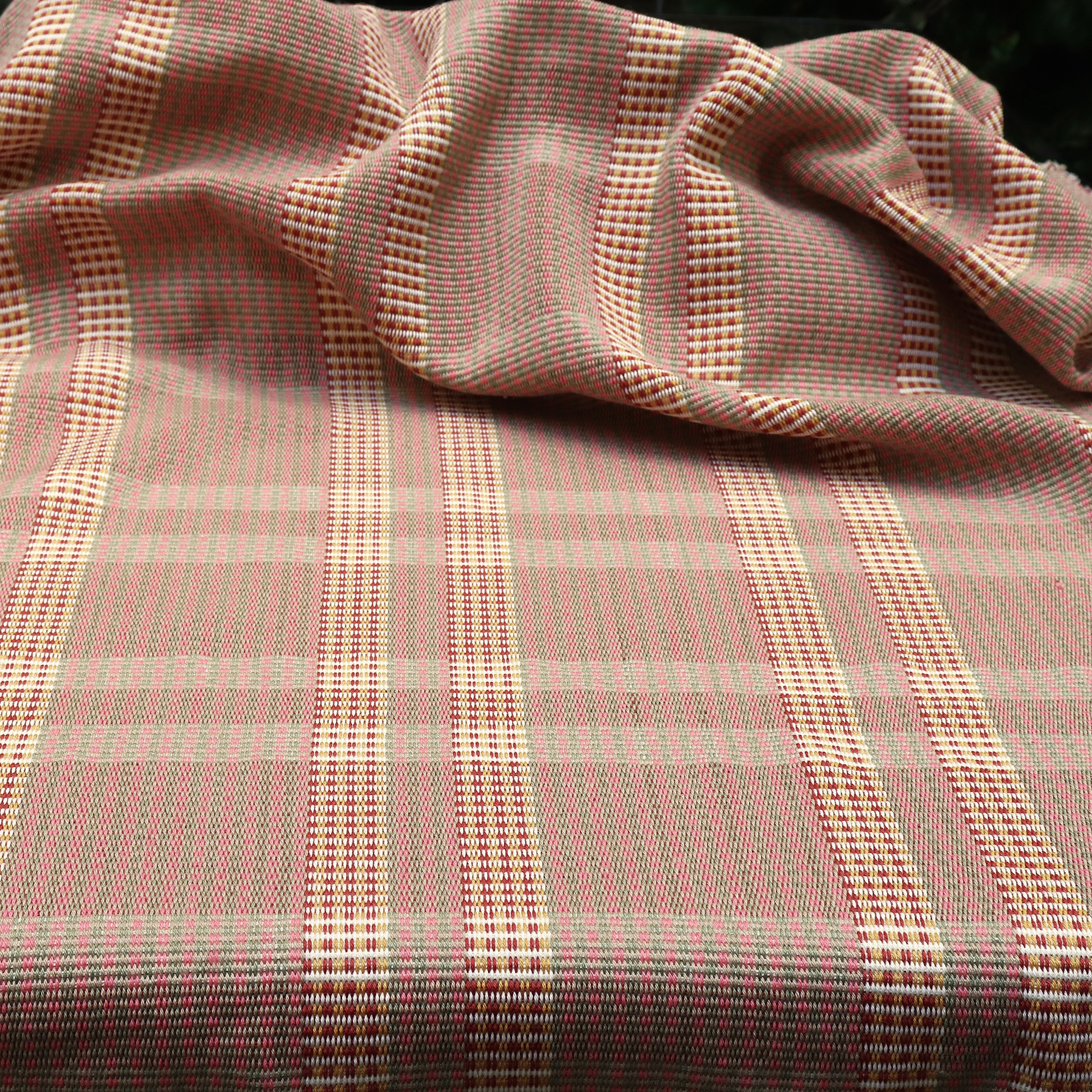 Handwoven fabric gently draped in a subtle window pane plaid in shades of red, pink sage green and cream. 