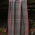 A handowven window pane fabric in brown and pink is draped in an outdoor setting. 