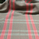 Handwoven fabric gently draped in a subtle window pane plaid in shades of red, pink, brown and cream. 