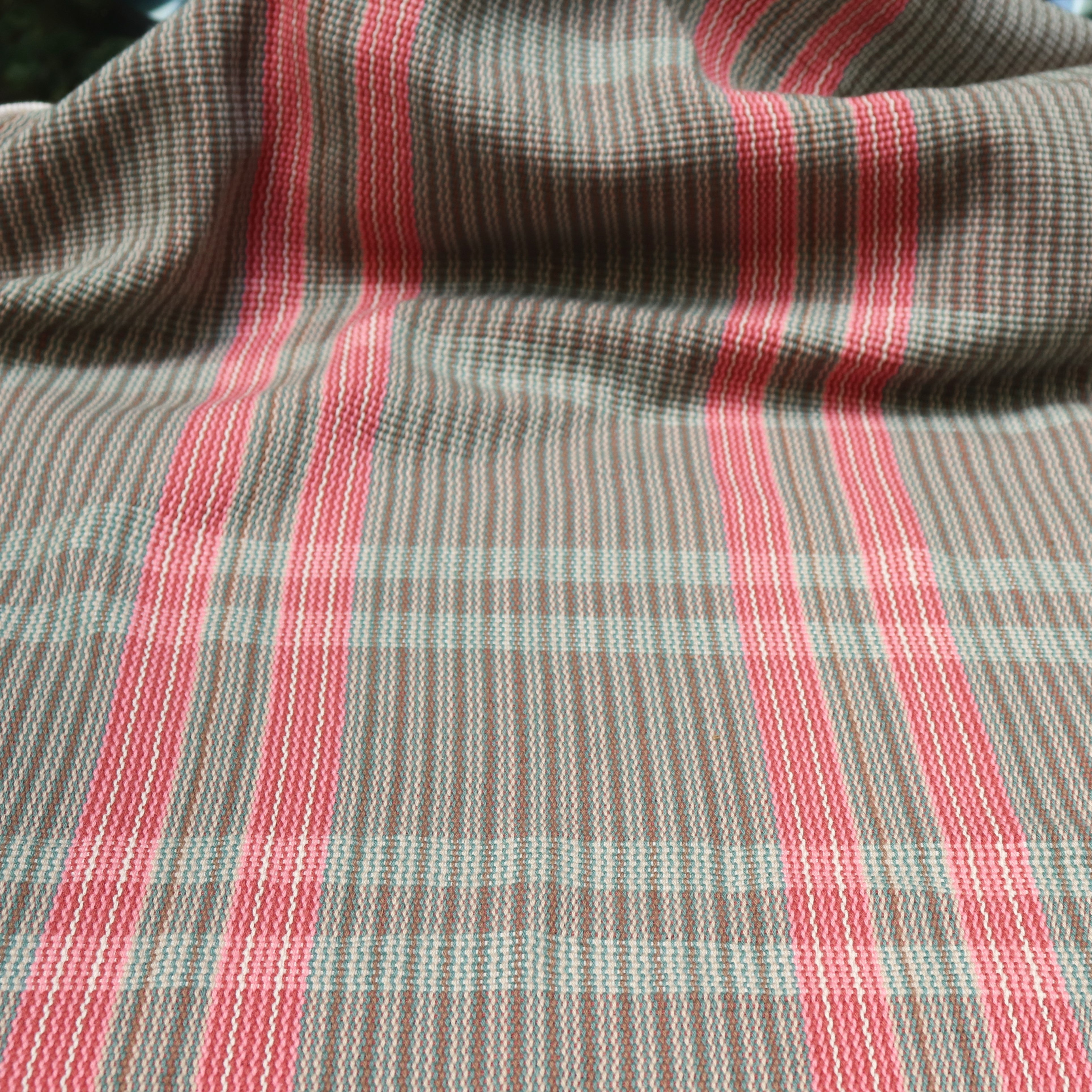 Handwoven fabric gently draped in a subtle window pane plaid in shades of red, pink, brown and cream. 