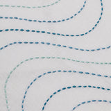 Detail of fabric with an undulating hand-embroidered pattern in shades of blue on a white field.