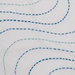 Detail of fabric with an undulating hand-embroidered pattern in shades of blue on a white field.