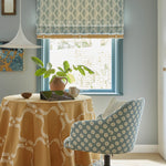 A dining room with a chair, tablecloth and curtains all upholstered in various floral and leaf prints in blue and yellow.