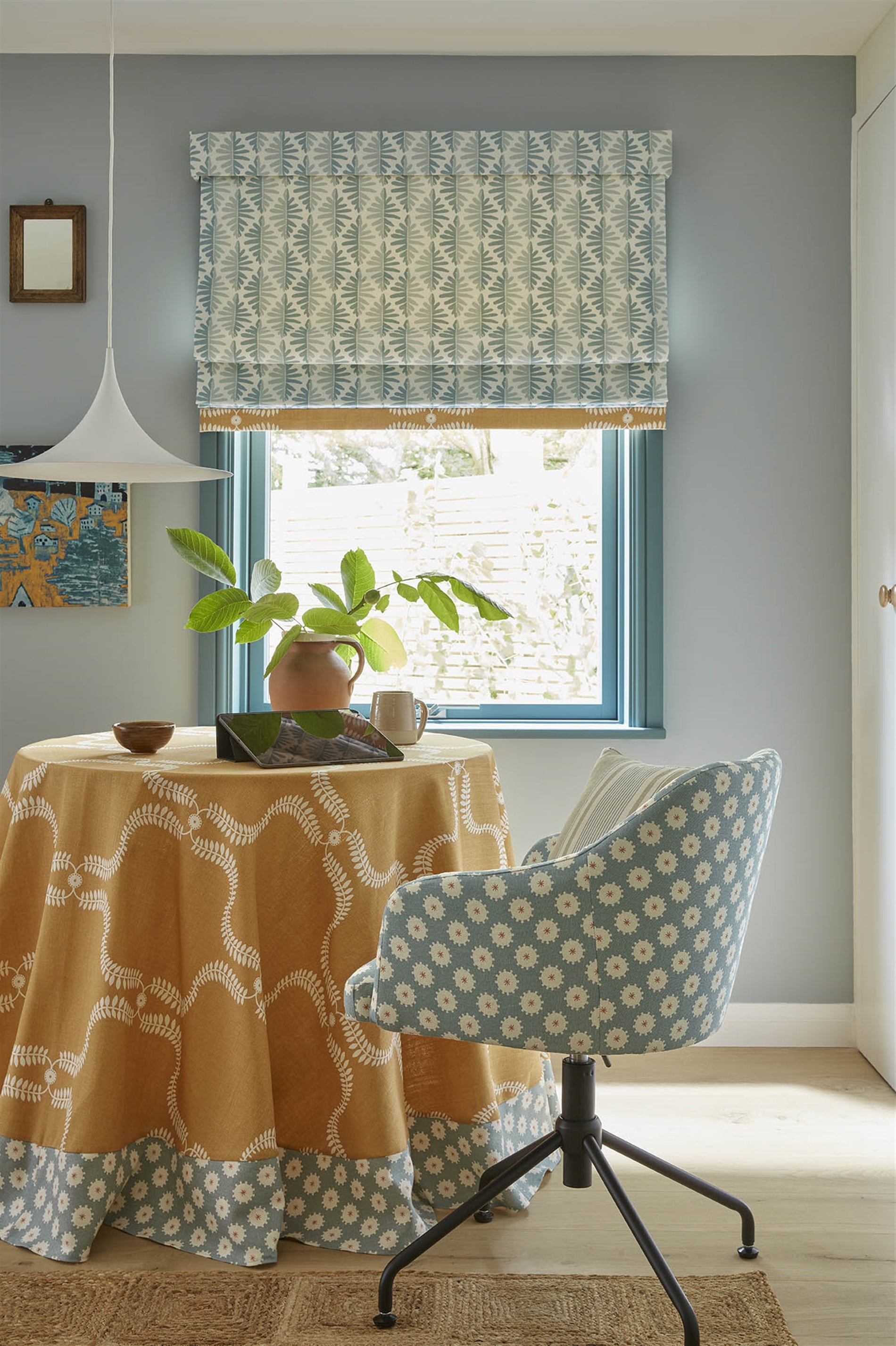 A dining room with a chair, tablecloth and curtains all upholstered in various floral and leaf prints in blue and yellow.