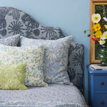 Bed with floral bedding and pillows against a blue wall, next to a blue nightstand with decorative items.