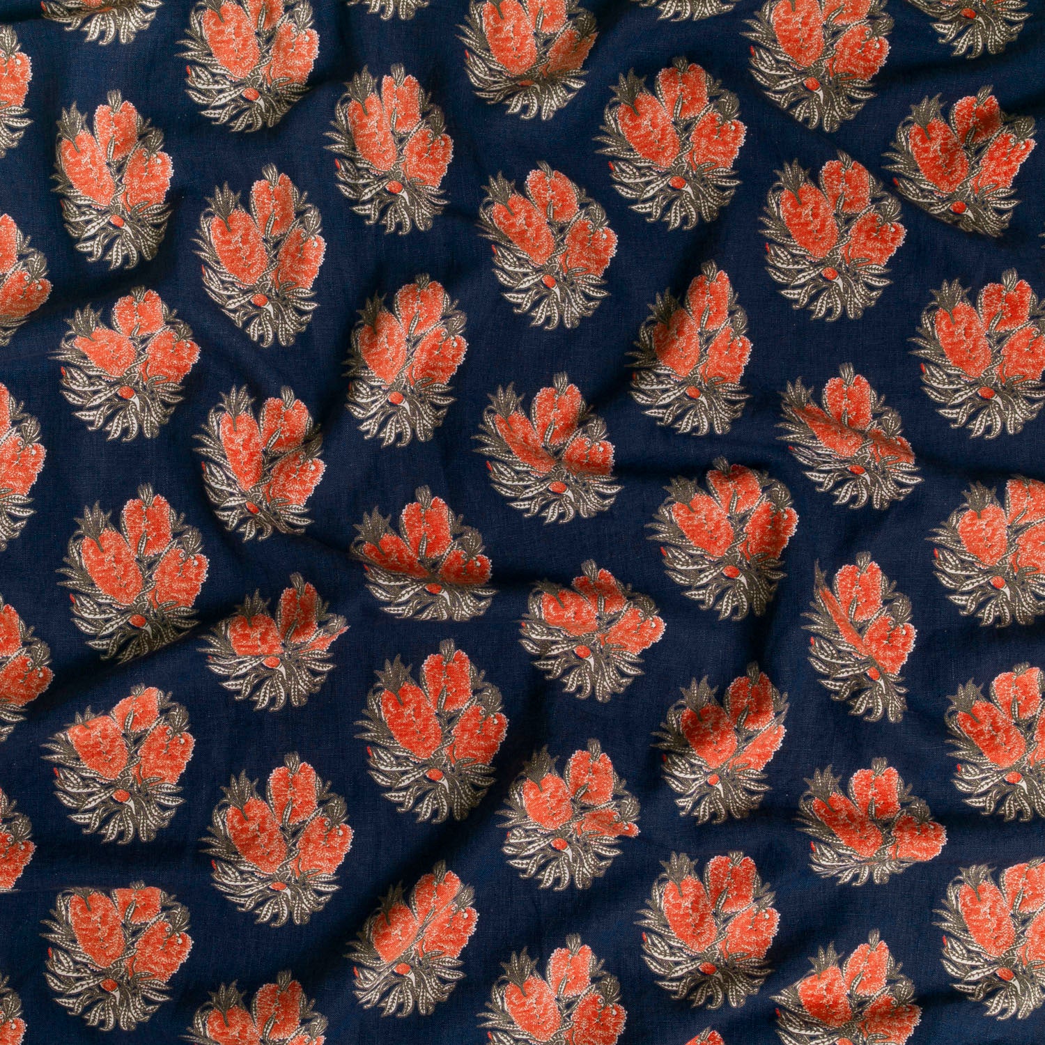 Draped fabric in a floral cameo print in tan and red on a navy field.