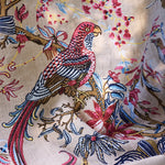 Printed fabric detail in a lyrical jungle design with tropical birds and leafy branches in pink, tan, blue and yellow on a beige field.