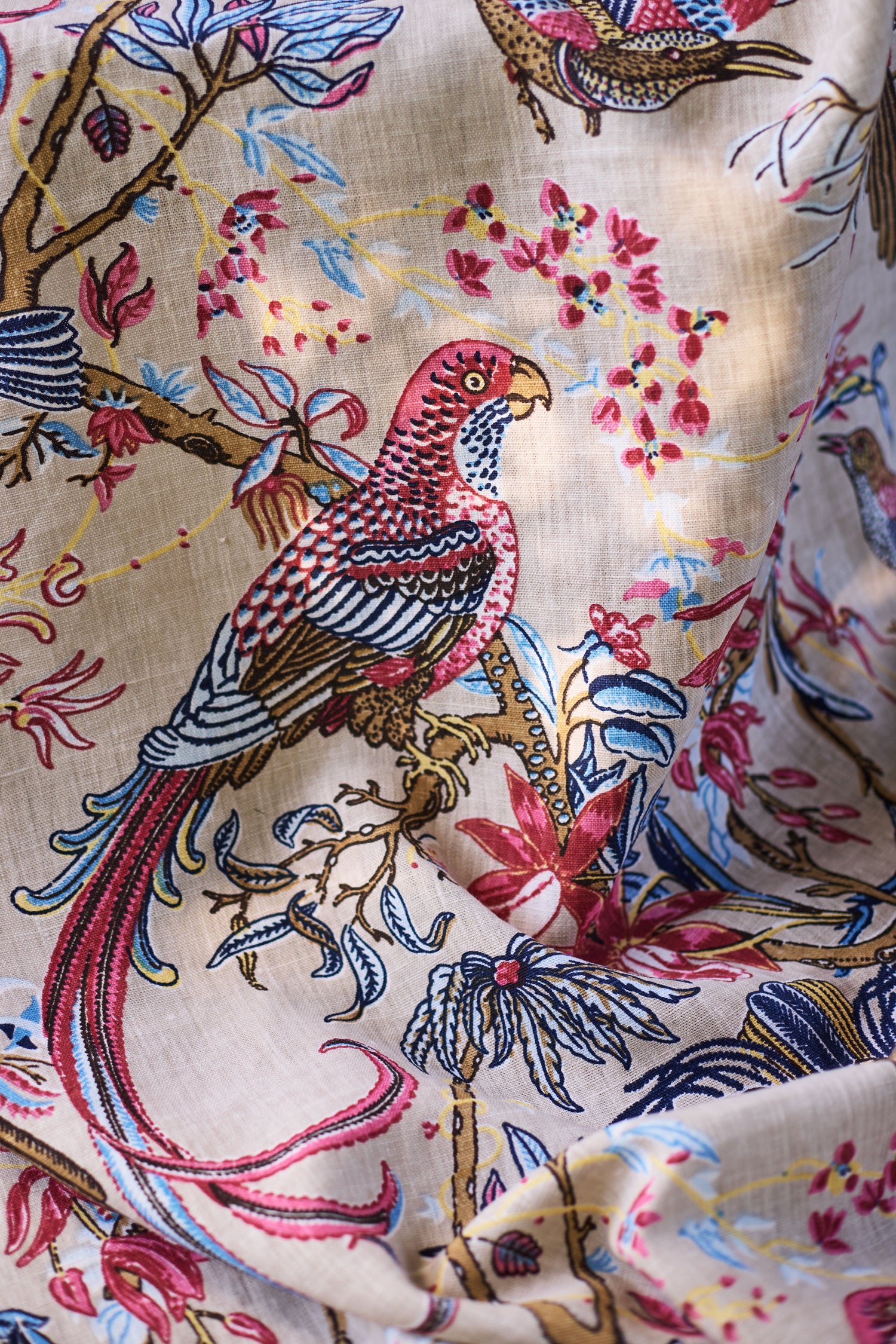 Printed fabric detail in a lyrical jungle design with tropical birds and leafy branches in pink, tan, blue and yellow on a beige field.