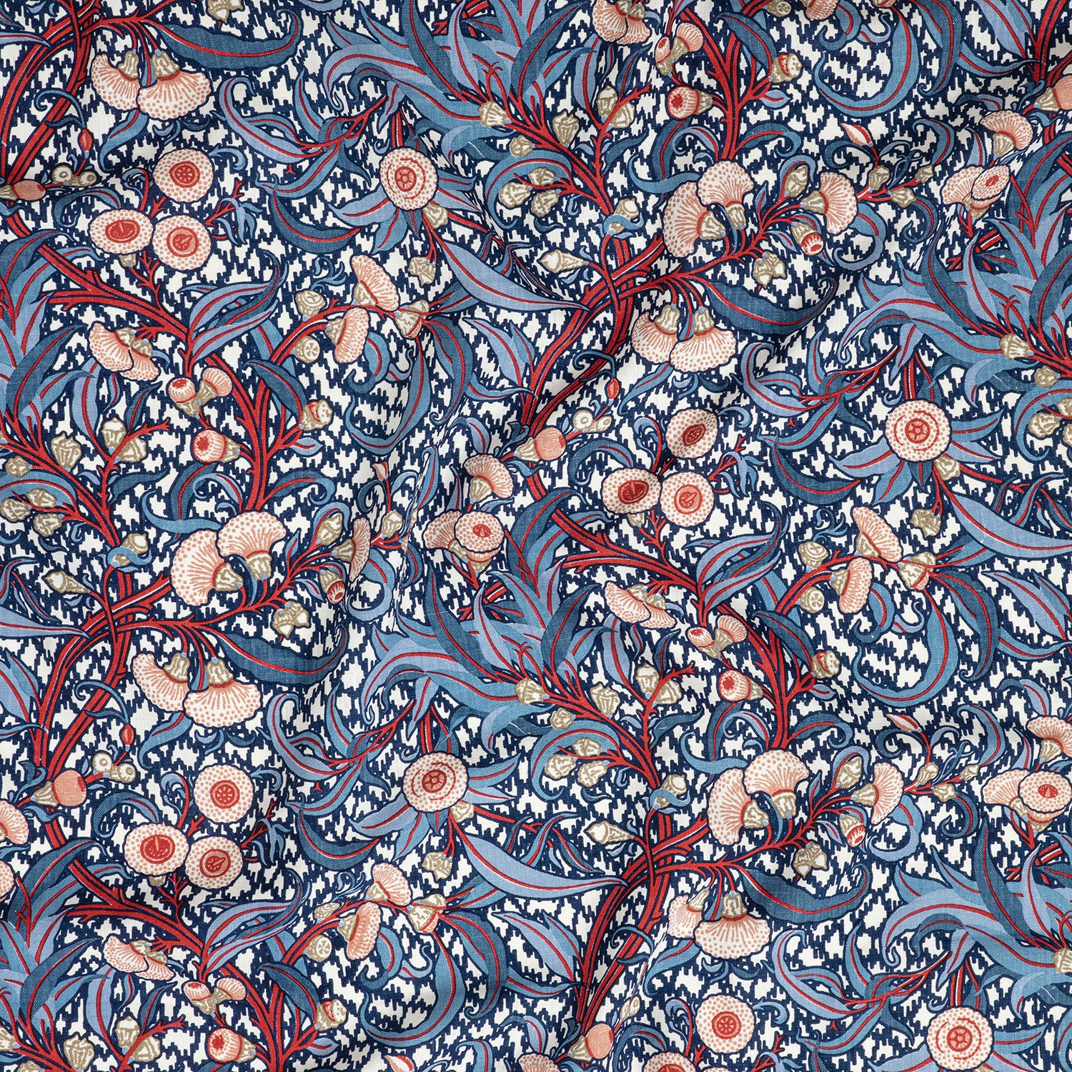 Draped fabric in a dense floral print in blue, red and orange on a cream field.