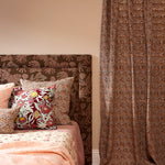 Bed with patterned headboard and pillows next to a curtain with a similar design.