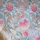 Printed fabric in a lush floral botanical design in red, pink, yellow green and turquoise on a tan field. 