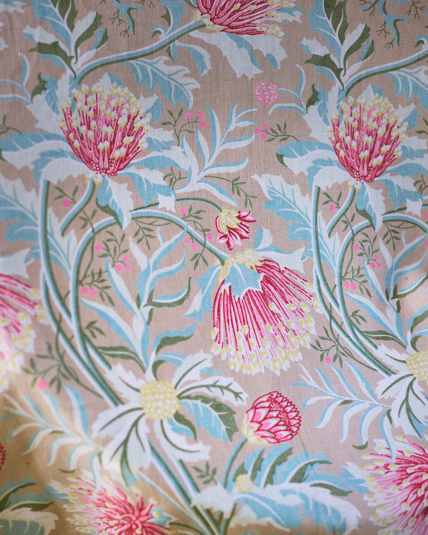 Printed fabric in a lush floral botanical design in red, pink, yellow green and turquoise on a tan field. 