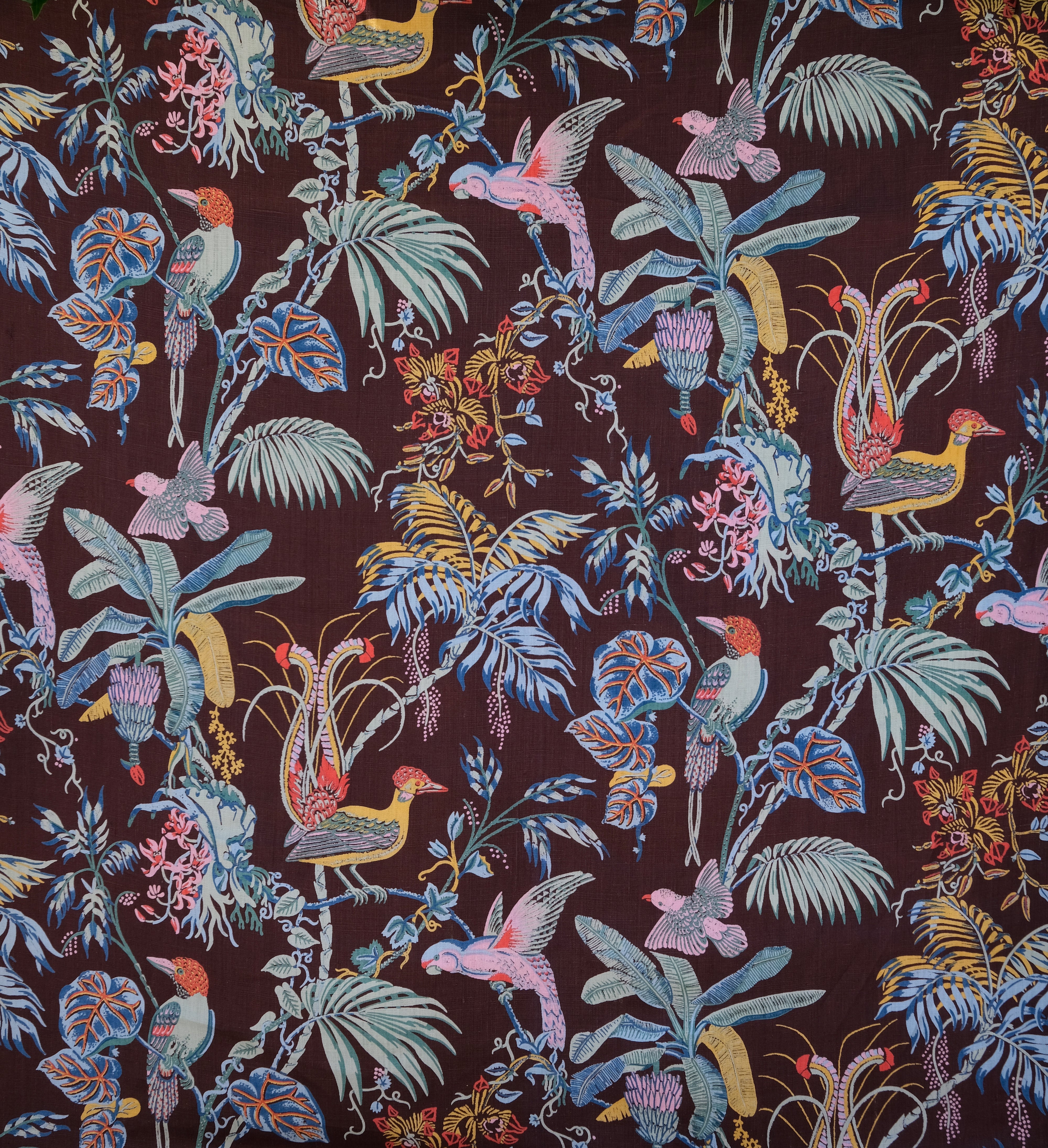 Detail of fabric in a dense leaf and bird print in a rainbow of shades on a dark brown field.