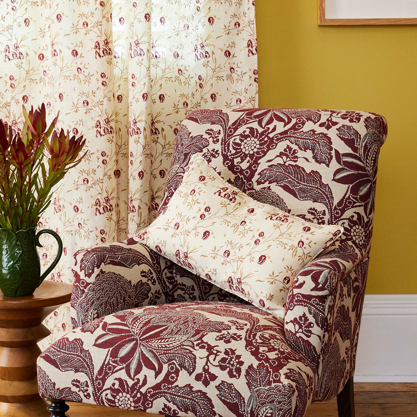 Floral-patterned armchair with a pillow against a yellow wall with a framed picture.