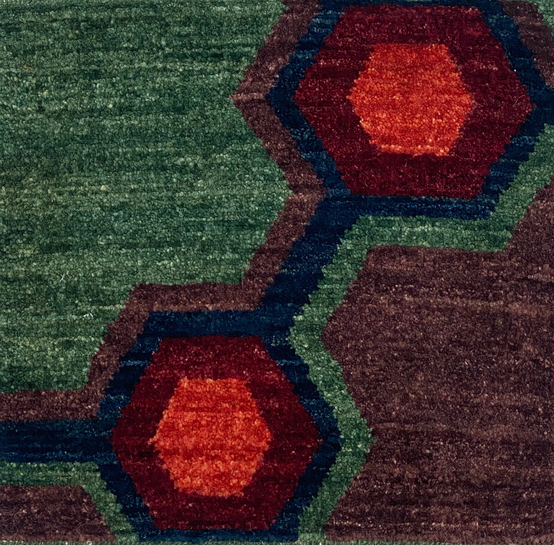 Handknotted carpet close up in a geometric design in green, blue, red and purple. 