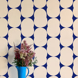 A vase of flowers stands in front of a wall papered in an abstract curvilinear pattern in cream on a navy field.