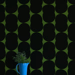 A vase of flowers stands in front of a wall papered in an abstract curvilinear pattern in gray on an olive field.