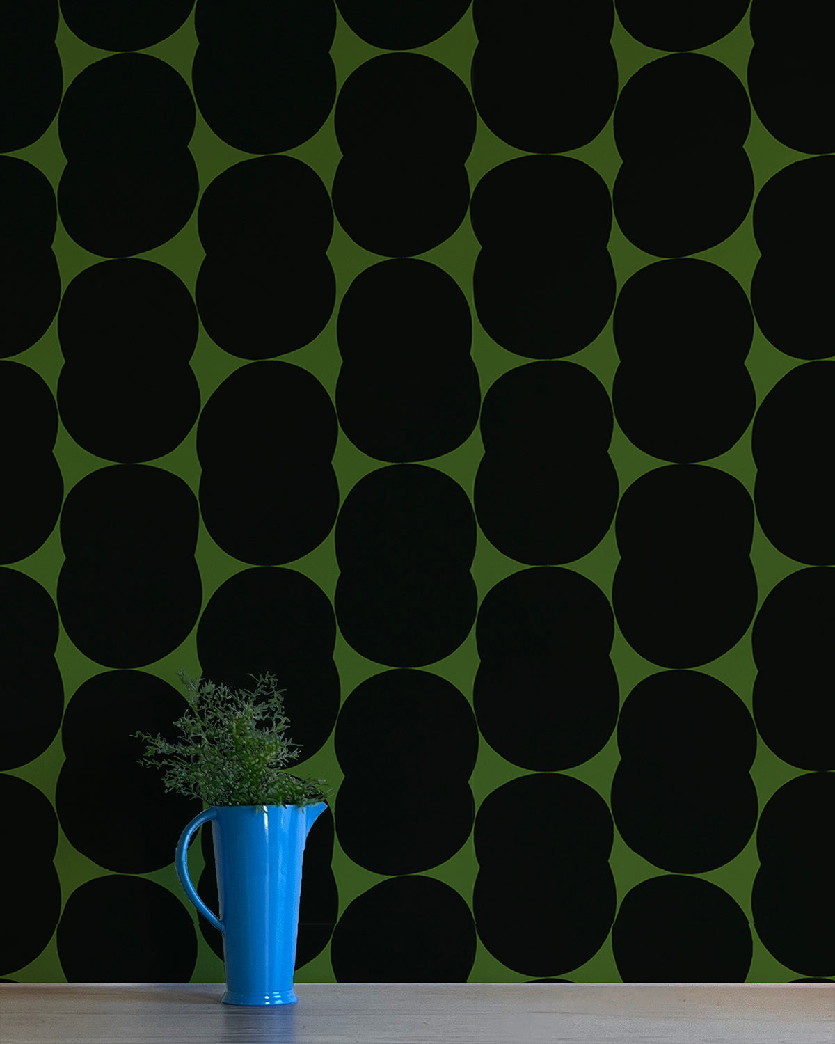 A vase of flowers stands in front of a wall papered in an abstract curvilinear pattern in gray on an olive field.