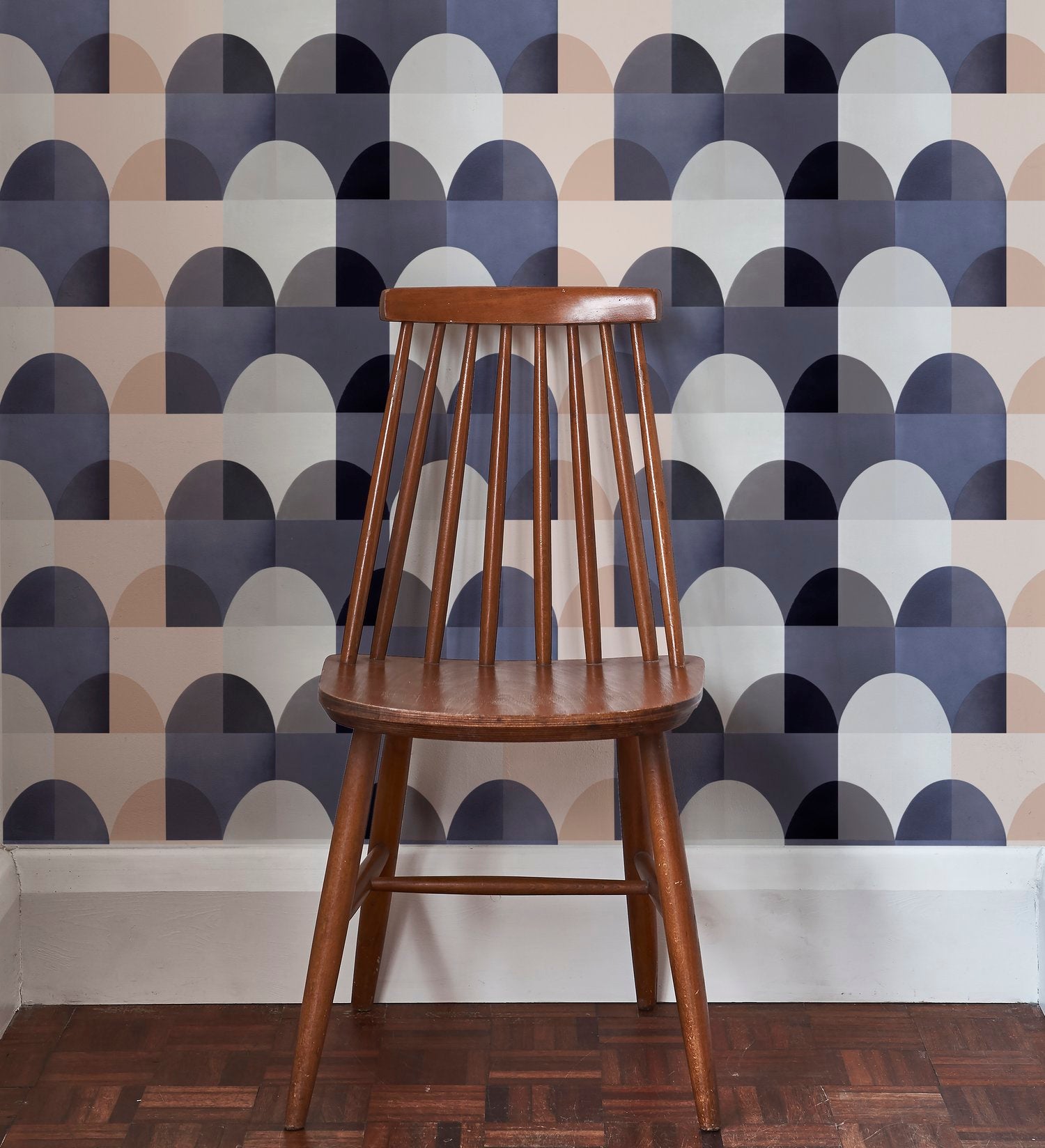 A wooden chair stands in front of a wall papered in a curvy geometric print in shades of white, tan, purple and gray.