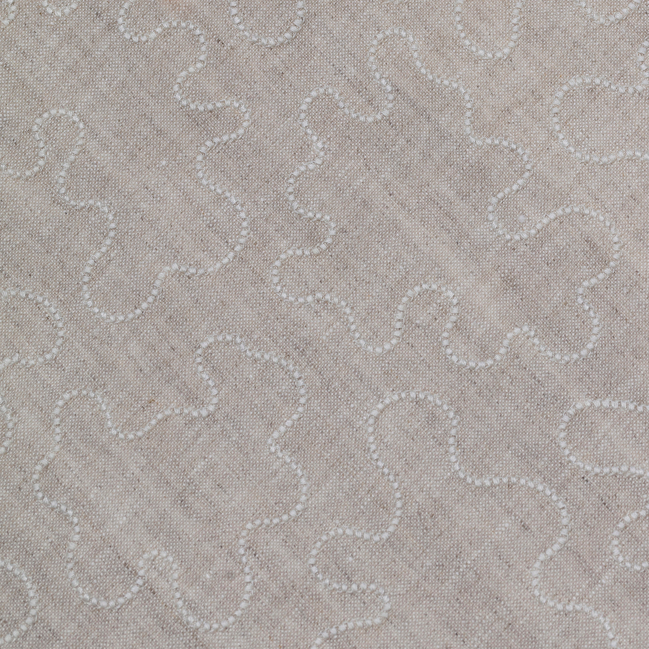 Fabric with an abstract embroidered pattern in white on a cream field.