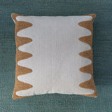 Square cream throw pillow with a wavy raffia embroidery pattern on the sides, laying on a turquoise fabric background.