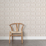 A wooden chair stands in front of a wall papered in a large-scale checked pattern in shades of cream and tan.