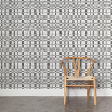 A wooden chair stands in front of a wall papered in a large-scale checked pattern in shades of gray and white.