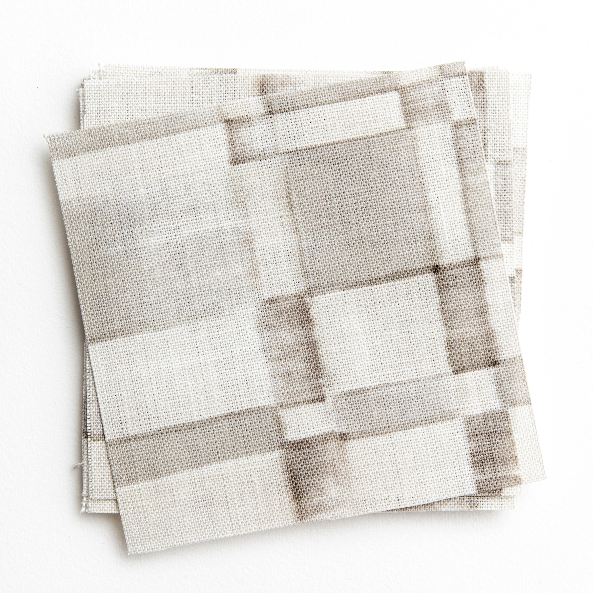 A stack of fabric swatches in a large-scale checked pattern in shades of greige.