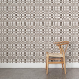 A wooden chair stands in front of a wall papered in a large-scale checked pattern in shades of greige and white.