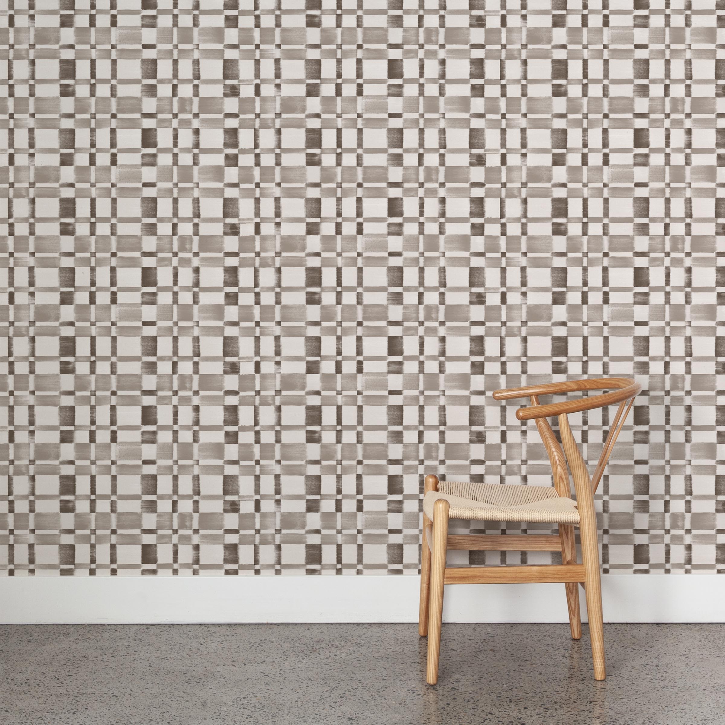 A wooden chair stands in front of a wall papered in a large-scale checked pattern in shades of greige and white.